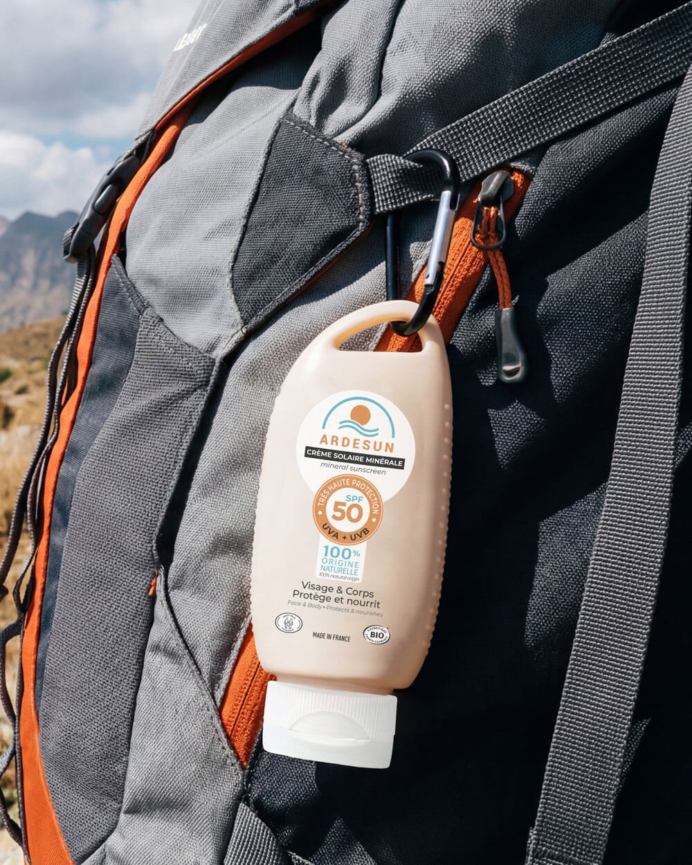 Mineral sunscreen SPF 50 ARDESUN clipped to a backpack with a carabiner, travel-size for hiking and outdoor activities