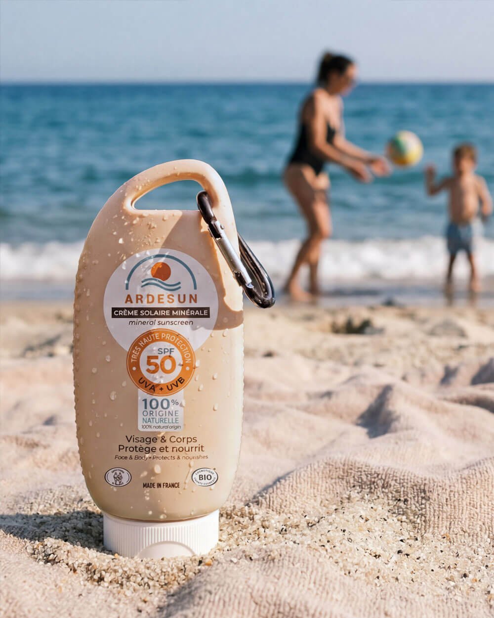 Crème solaire minérale SPF 50 ARDESUN sur la plage avec enfants en arrière-plan, protection solaire visage et corps
