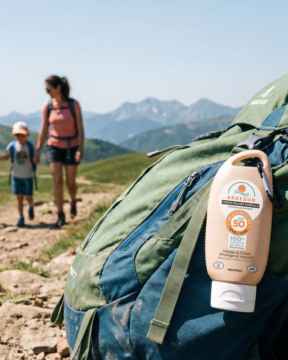 Crème solaire minérale SPF 50 ARDESUN accrochée à un sac de randonnée avec mousqueton en montagne